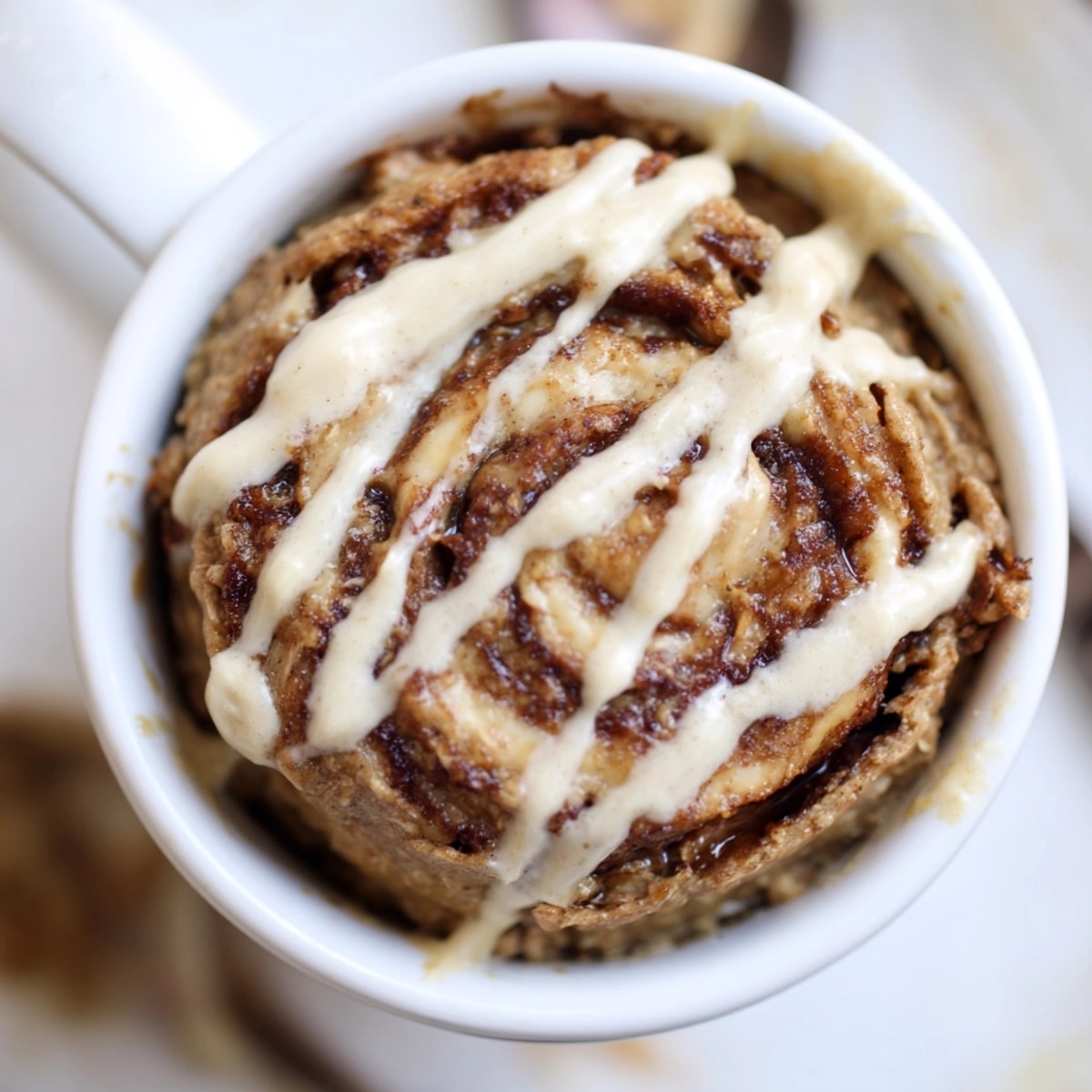 Warm, fluffy Protein Cinnamon Roll Mug Cake drizzled with creamy frosting, ready to eat.