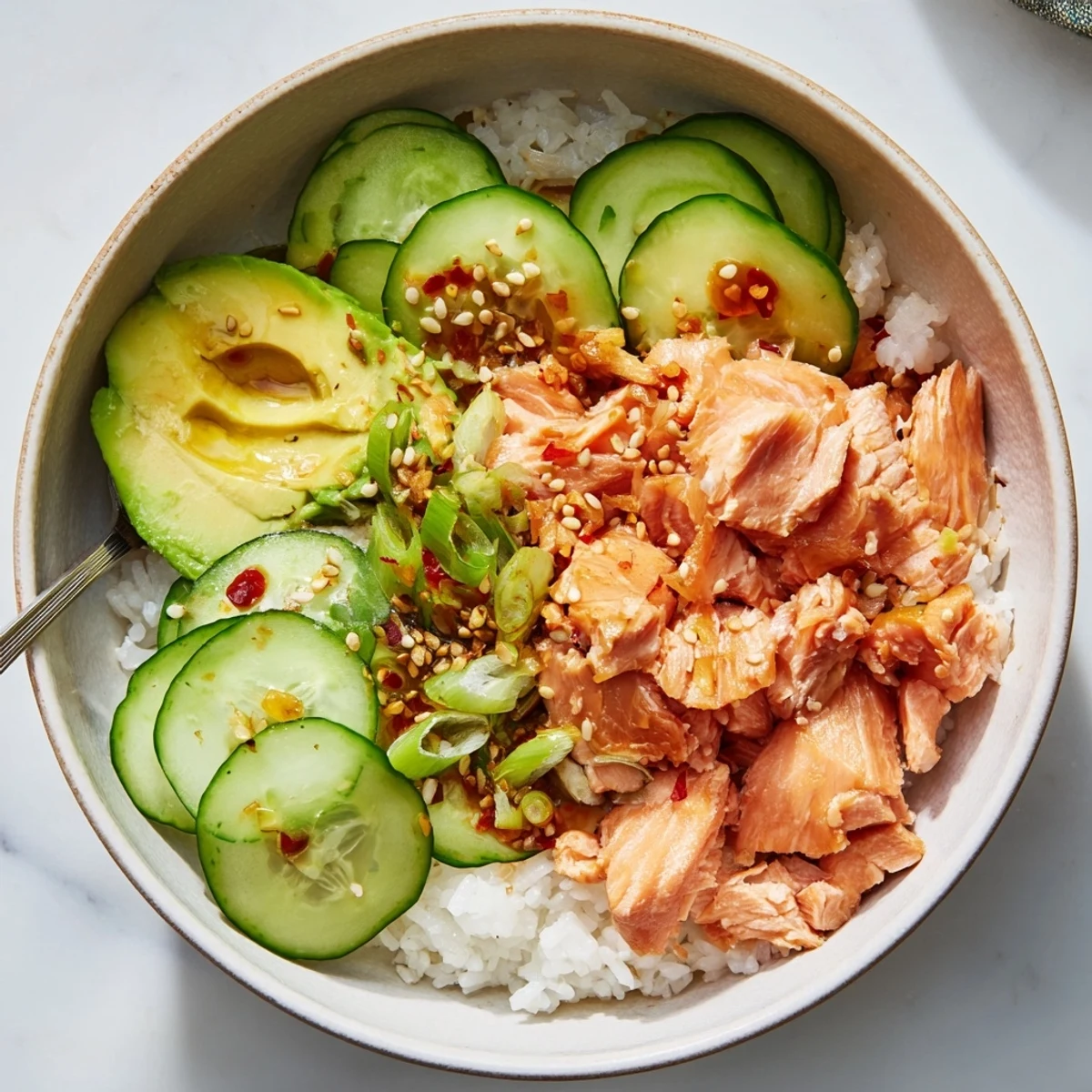 A vibrant leftover salmon and rice bowl topped with fresh cucumber and avocado slices.  