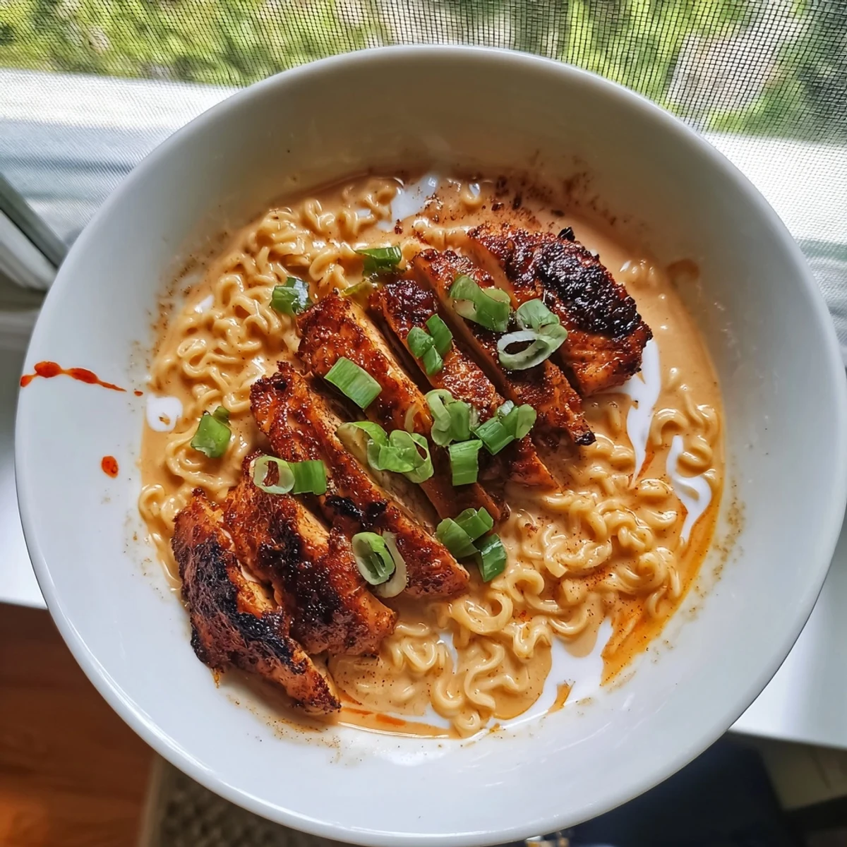 Steaming bowl of Fiery Chicken Ramen, showcasing tender chicken and a luscious, creamy garlic broth topped with green onions.