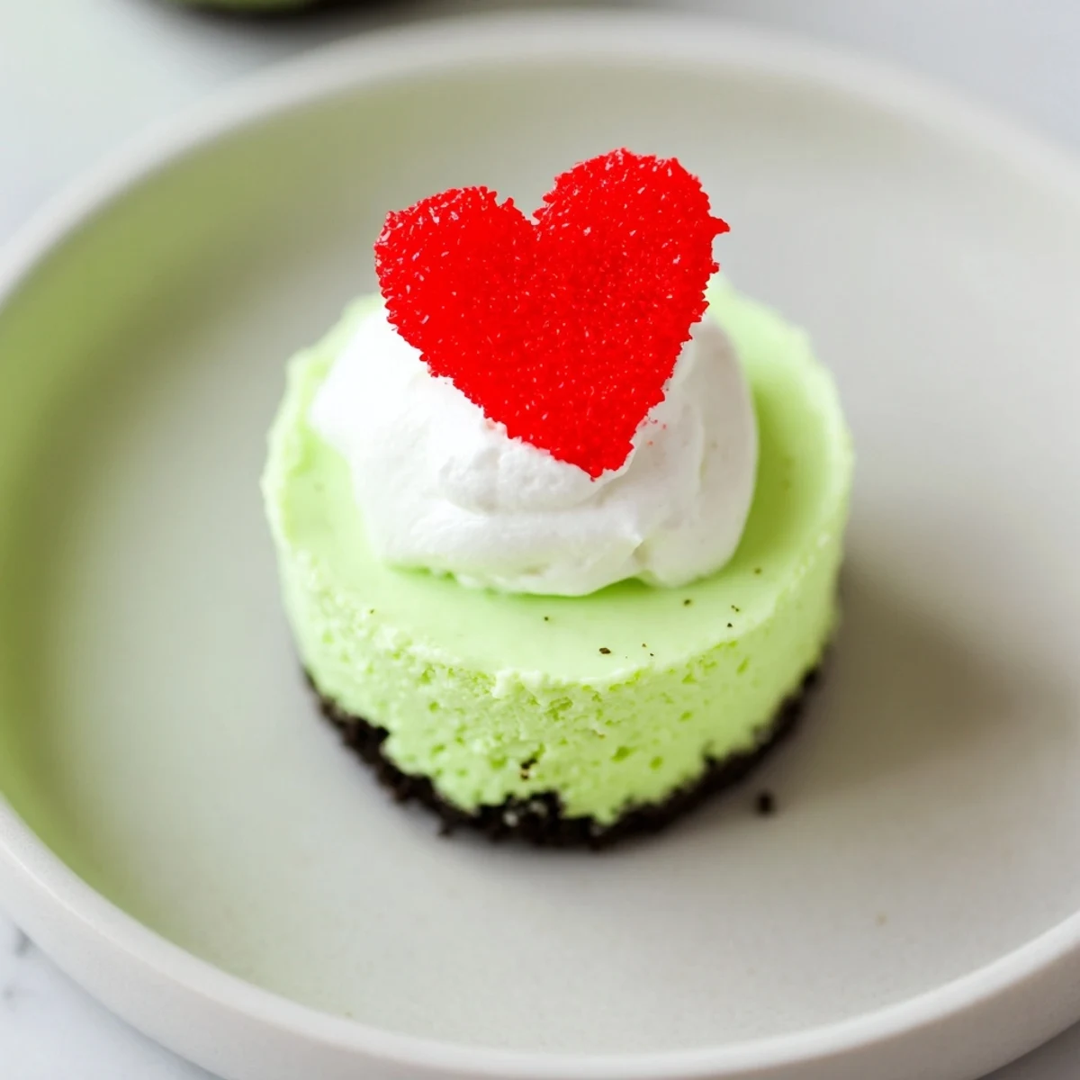 Vibrant green Grinch Mini Cheesecakes, topped with whipped cream and festive sprinkles, ready to serve and enjoy.