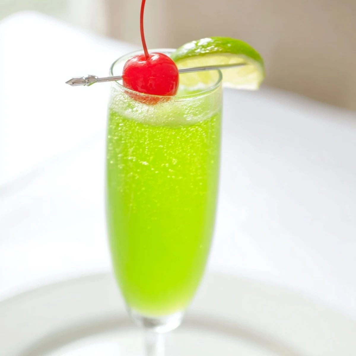 Bright green Quick Grinch Mimosa Mocktail, bubbly and festive, garnished with a cherry and lime slice.