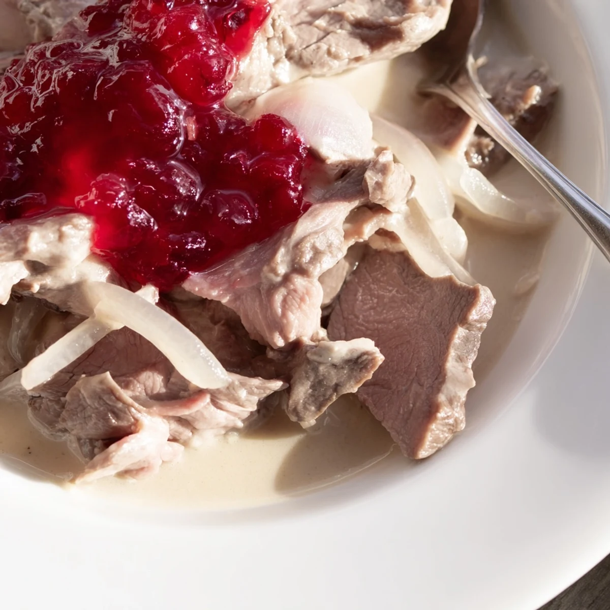 A close-up of a steaming bowl of Finnish reindeer stew, topped with tart lingonberry preserves.