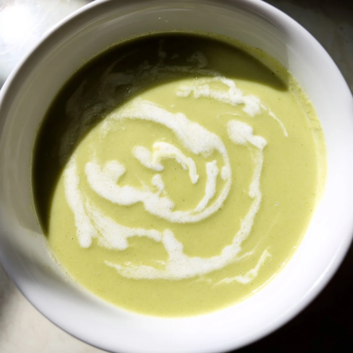 Vibrant green creamy broccoli soup garnished with chives and a drizzle of cream, highlighting its velvety texture in a warm pot.