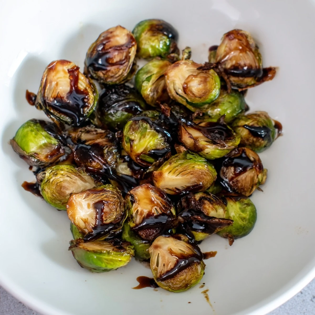 Golden-brown roasted Brussels sprouts glistening with a dark, sticky balsamic glaze on a rustic wooden platter.