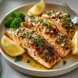 A plate of salmon with lemon wedges on top.