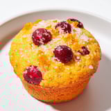 A close-up of fluffy quick festive cranberry orange muffins overflowing with cranberries ready to eat.