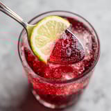 A glass of red drink with a slice of lemon.