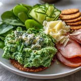 Kid-friendly green eggs and ham snack plate with crackers, spinach, and cucumber for a playful, nutritious treat.