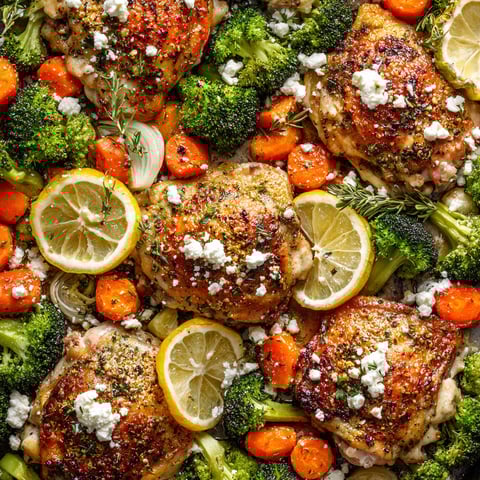 A close up of a chicken breast with feta cheese and lemon wedges.