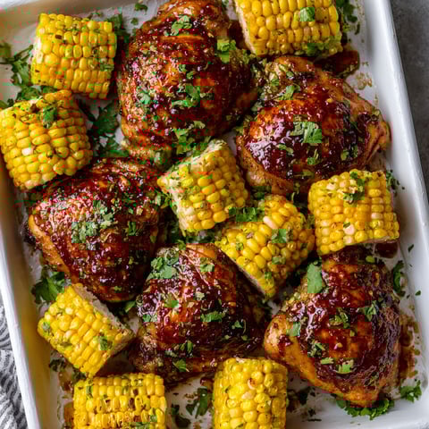 A dish of chicken with corn on the cob and a sauce.