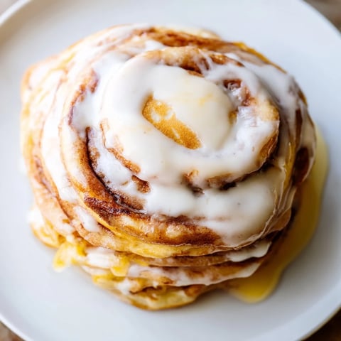 Golden-brown Cinnamon Roll Pancakes drizzled with sweet cream cheese frosting, a delightful brunch dish.