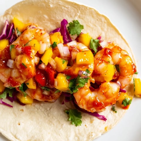 Warm tortillas filled with juicy Sriracha Shrimp Tacos topped with vibrant mango salsa, crunchy red cabbage, and fresh lime wedges.