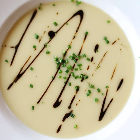 A bowl of creamy Celery Root Bisque garnished with fresh chives and a drizzle of cream, ready to serve.  