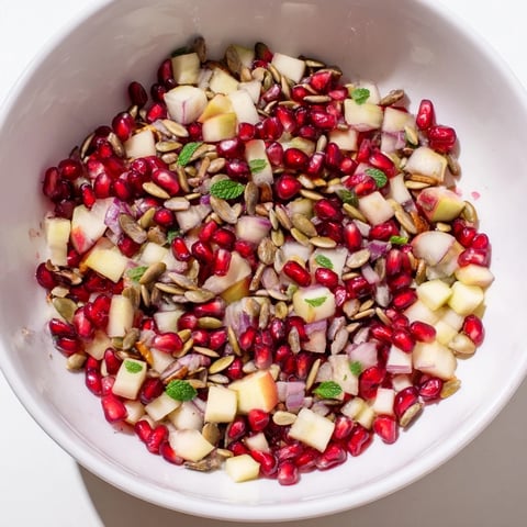 Vibrant Pomegranate and Walnut Salad in a white bowl, with red arils, diced apples, and toasted walnuts glistening with a light lemon-honey dressing.