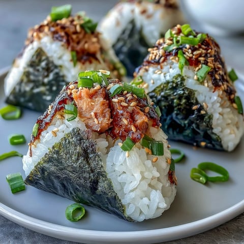 Spicy tuna onigiri featuring tender rice balls stuffed with zesty tuna filling and wrapped in crisp nori seaweed.  