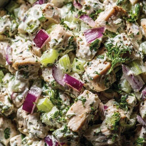 A close up of a salad with chicken, onions, and cucumbers.