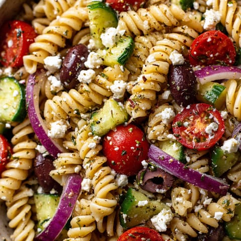 A bowl of pasta salad with tomatoes, cucumbers, olives, and feta cheese.