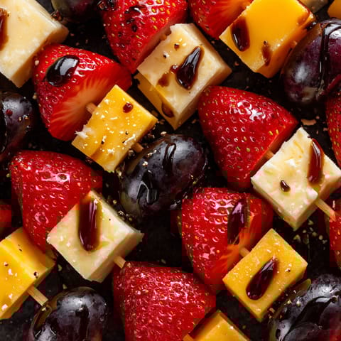 A close up of a plate of fruit and cheese skewers.