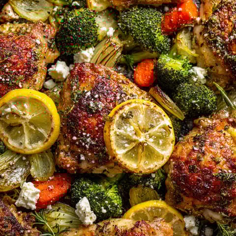 A close up of a plate of food with chicken, broccoli, carrots, and lemon wedges.