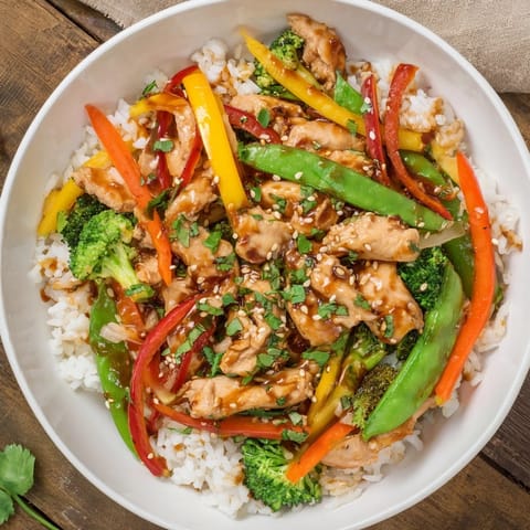 A flavorful bowl of Chicken Stir-Fry steaming, garnished with sesame seeds and fresh scallions on rice.
