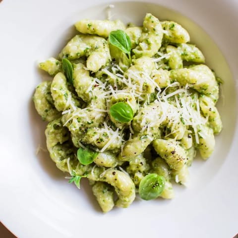 Bowl of Creamy Avocado Pesto Mac, topped with grated Parmesan and fresh basil leaves, ready to eat.