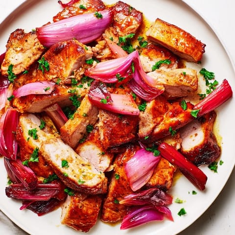 Tender pork and caramelized rhubarb pieces with zesty orange and fresh parsley garnish on a rustic traybake.