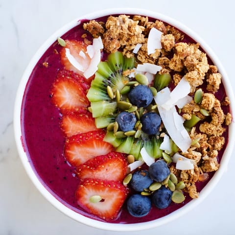 A vibrant bowl of Beet and Berry Smoothie Bowl garnished with fresh mint, coconut, and berries, ready for a quick snack.