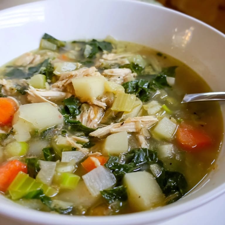 Close-up view of Collard Greens, Chicken and Vegetable Soup, highlighting vibrant green leaves and diced carrots floating in the hearty liquid.