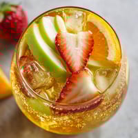 A glass of fruit juice with a slice of apple and strawberry.