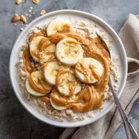 A bowl of oatmeal with bananas and peanut butter.