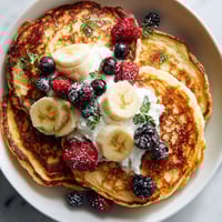 A plate of pancakes with bananas and berries on top.