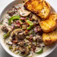A bowl of soup with mushrooms and bread.