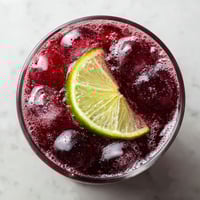 A glass of red wine with a slice of lime in it.