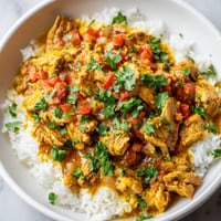 A bowl of rice with meat and tomatoes.